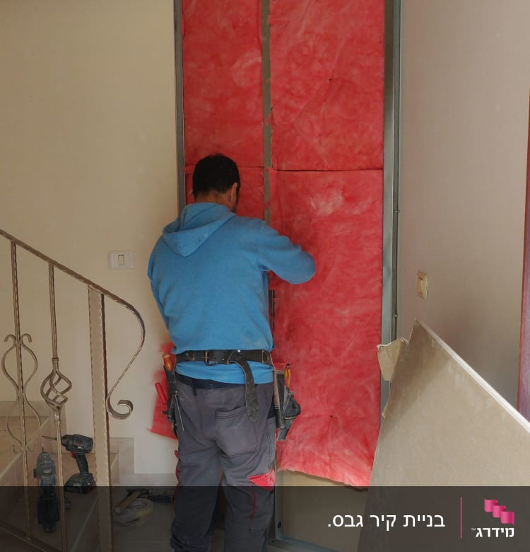 אדם מתקין לוחות גבס על קיר עם בידוד אדום